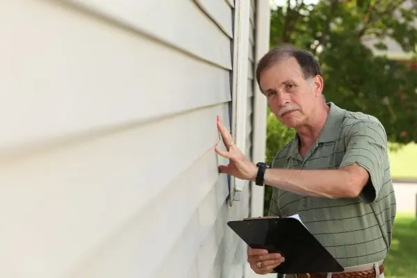 adult male with clipboard inspects vinyl siding on residential home