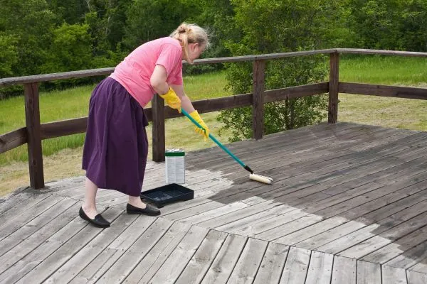 woman waterproofing wooden outdoor deck